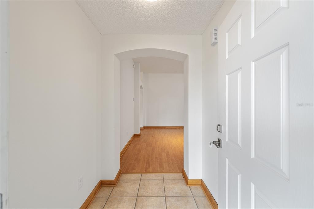 An entryway with tiled flooring leads through an arched doorway into a wood-floored living area — 1928 PEACHTREE AVENUE, THE VILLAGES, FL