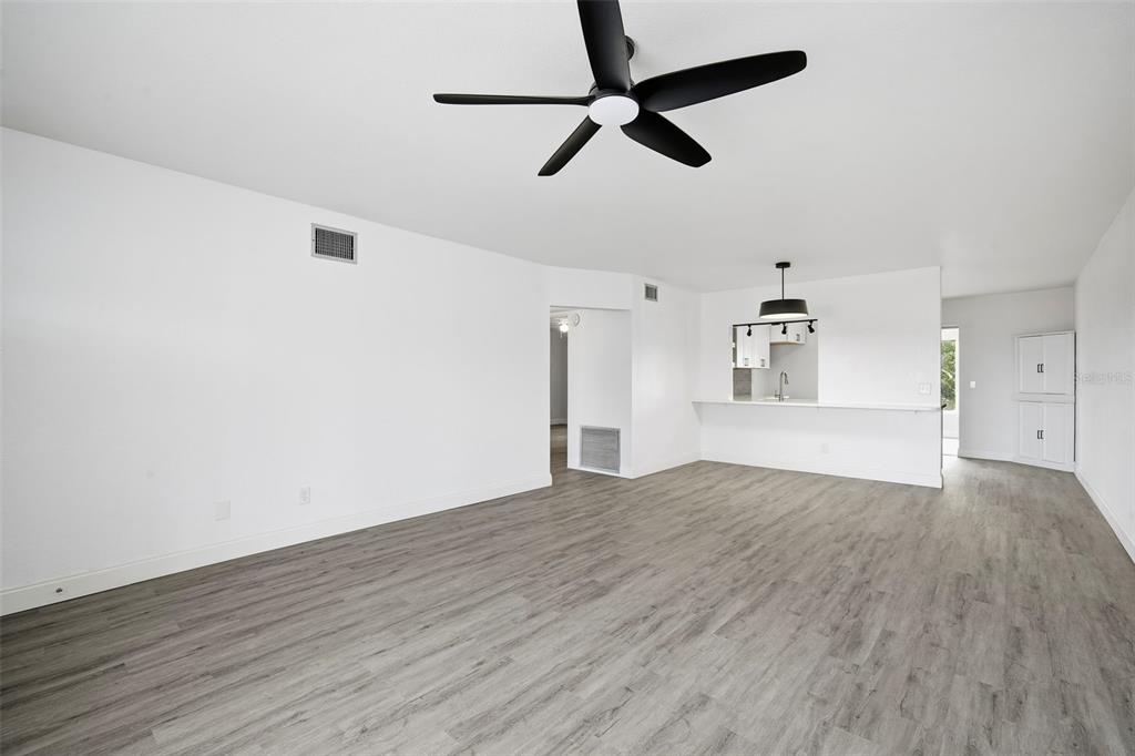 A bright, open-concept living area features gray wood-look flooring, white walls, and a ceiling fan — 2431 CANADIAN WAY UNIT 47, CLEARWATER, FL