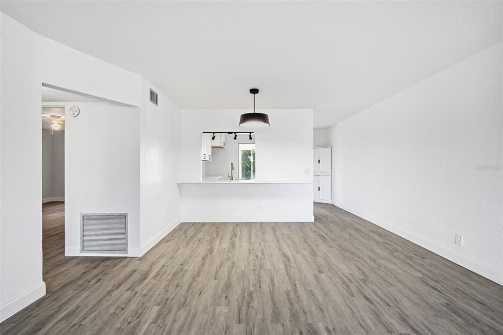 An empty living room with gray wood-look flooring, white walls, and a kitchen pass-through window — 2431 CANADIAN WAY UNIT 47, CLEARWATER, FL