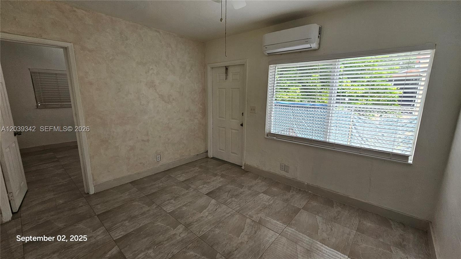 A room with tiled floors, a textured wall, a window with blinds, and a wall-mounted AC — 1830 Monroe St # 1834, Hollywood FL 33020, HOLLYWOOD, FL