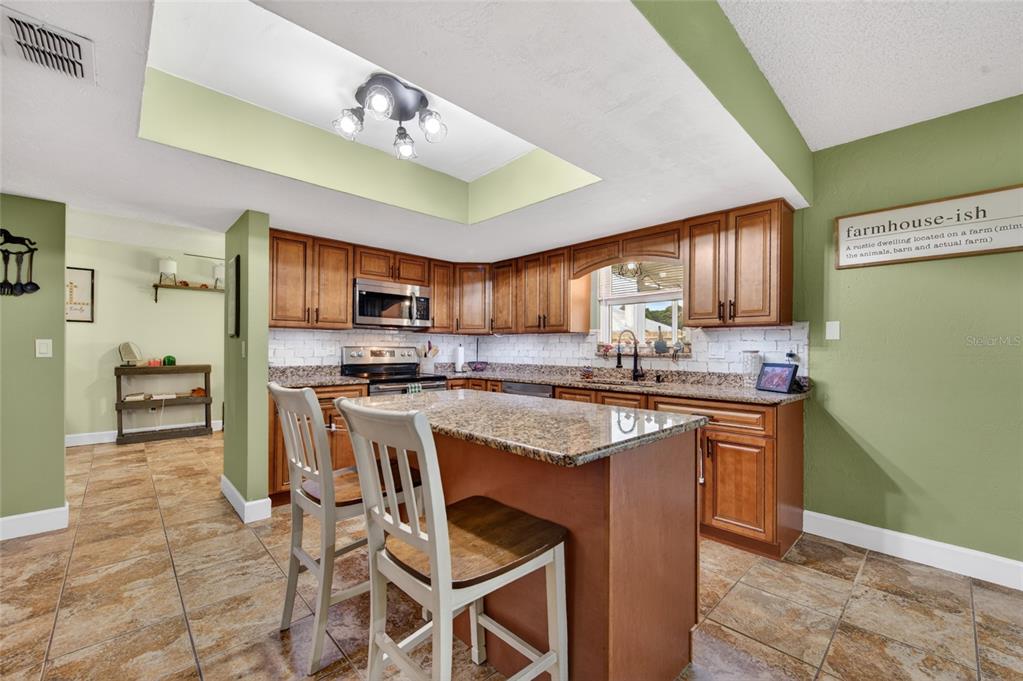 A kitchen features wood cabinets, granite countertops, a central island, and green painted walls — 222 PINEROCK PLACE, PORT ORANGE, FL
