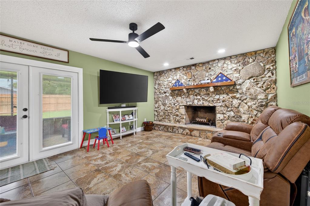 A living room features a stone fireplace, tile flooring, a ceiling fan, and a television — 222 PINEROCK PLACE, PORT ORANGE, FL