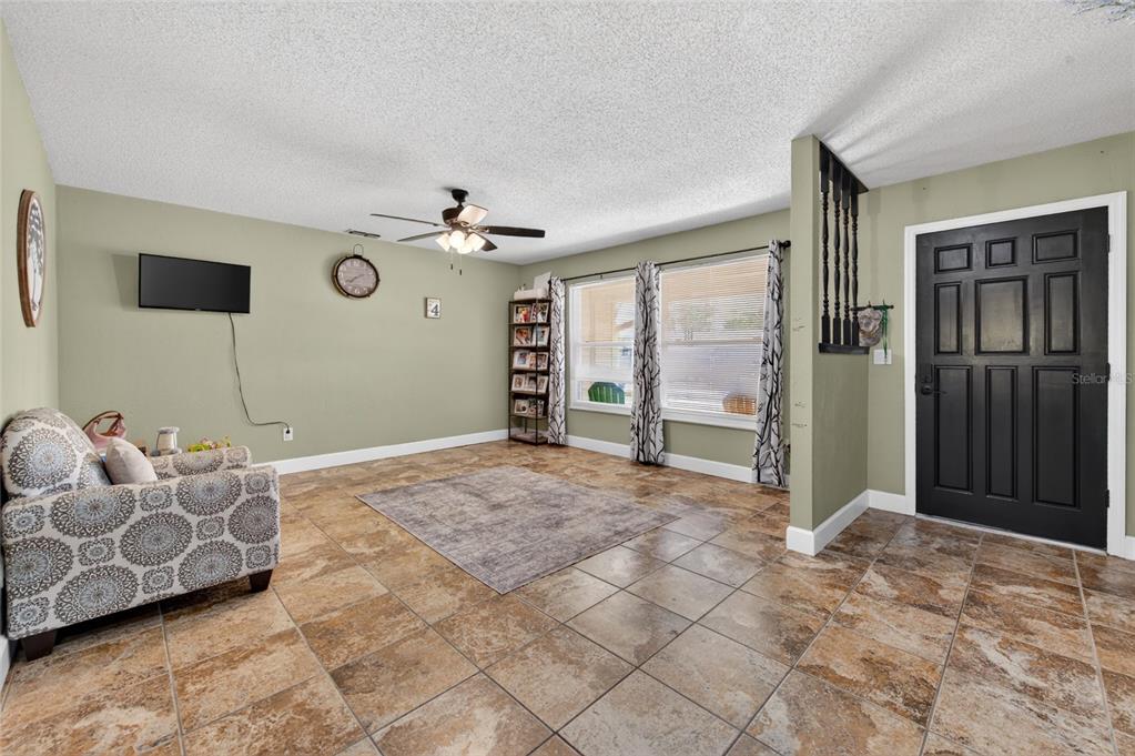 A living room with tiled floors, a ceiling fan, and a black front door — 222 PINEROCK PLACE, PORT ORANGE, FL