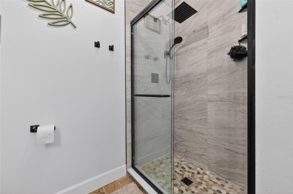 A bathroom features a glass-enclosed shower with pebble flooring and a black rainfall showerhead — 222 PINEROCK PLACE, PORT ORANGE, FL