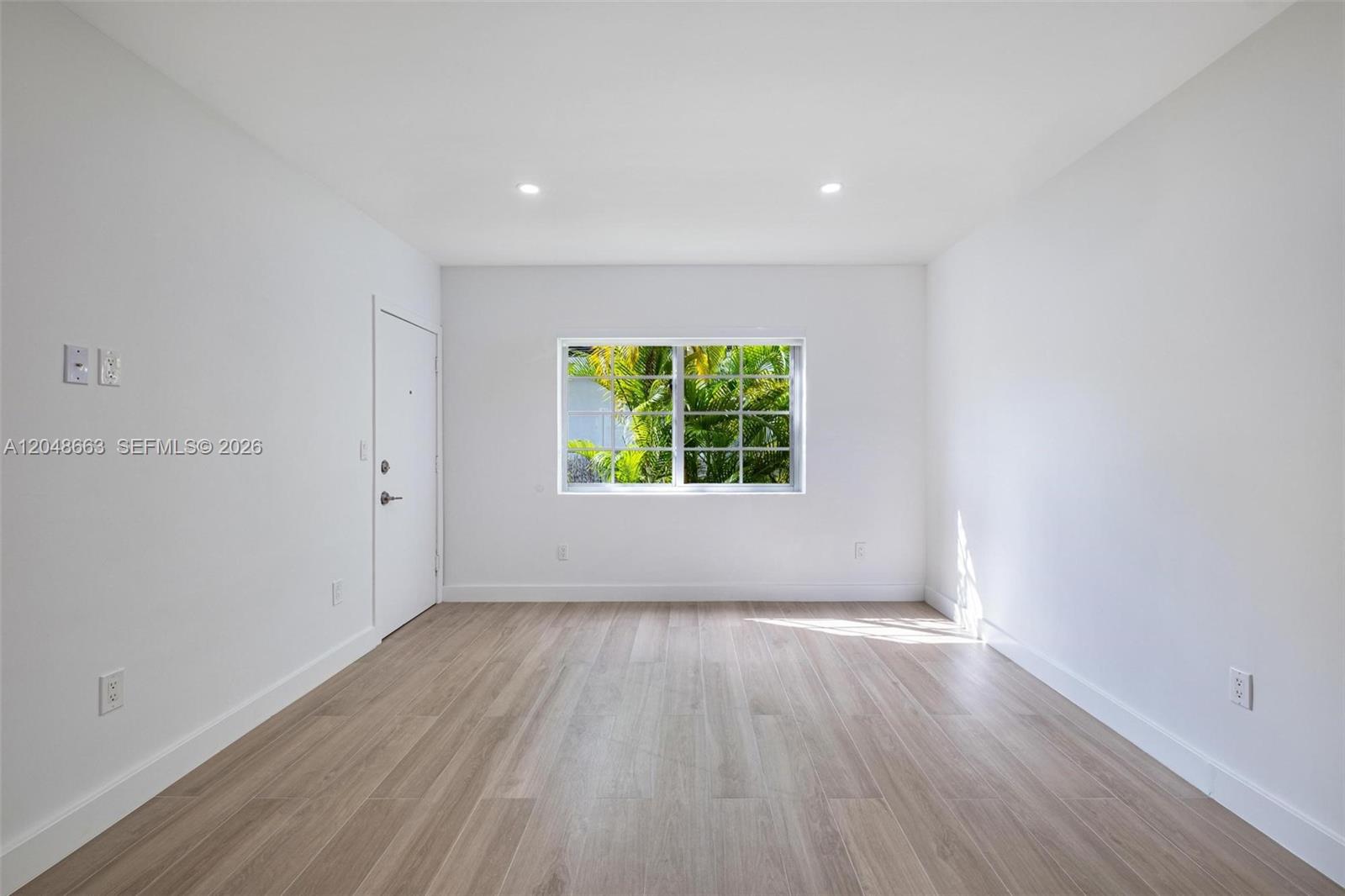 An empty room features white walls, light wood-look flooring, a window, and a white door — 1610 Michigan Ave # 2, Miami Beach FL 33139, MIAMI BEACH, FL