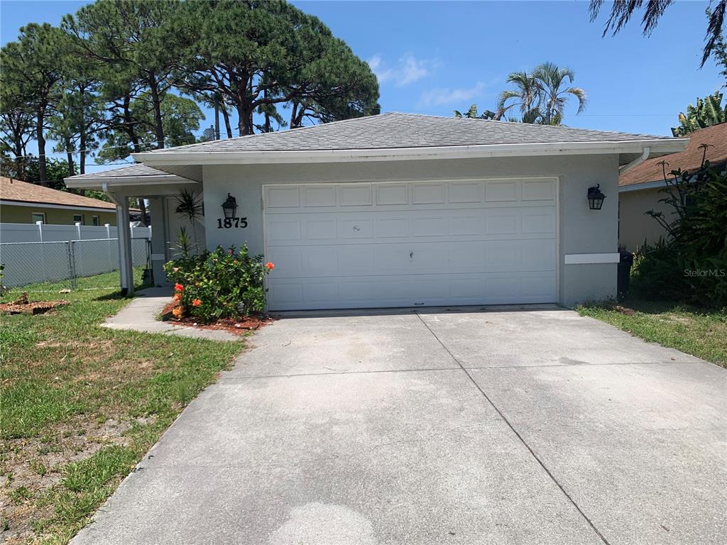 A gray single-story house features a white garage door and a concrete driveway — 1875 VAMO DRIVE, SARASOTA, FL