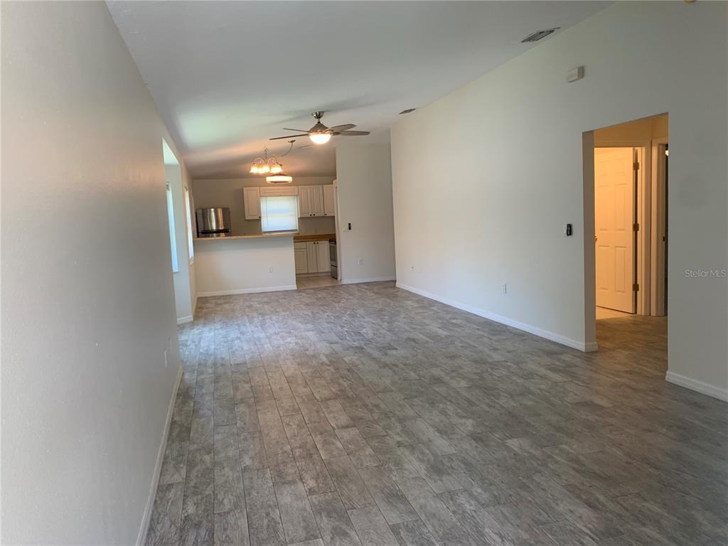 An open-concept living area features light gray wood-look tile flooring and a kitchen beyond — 1875 VAMO DRIVE, SARASOTA, FL