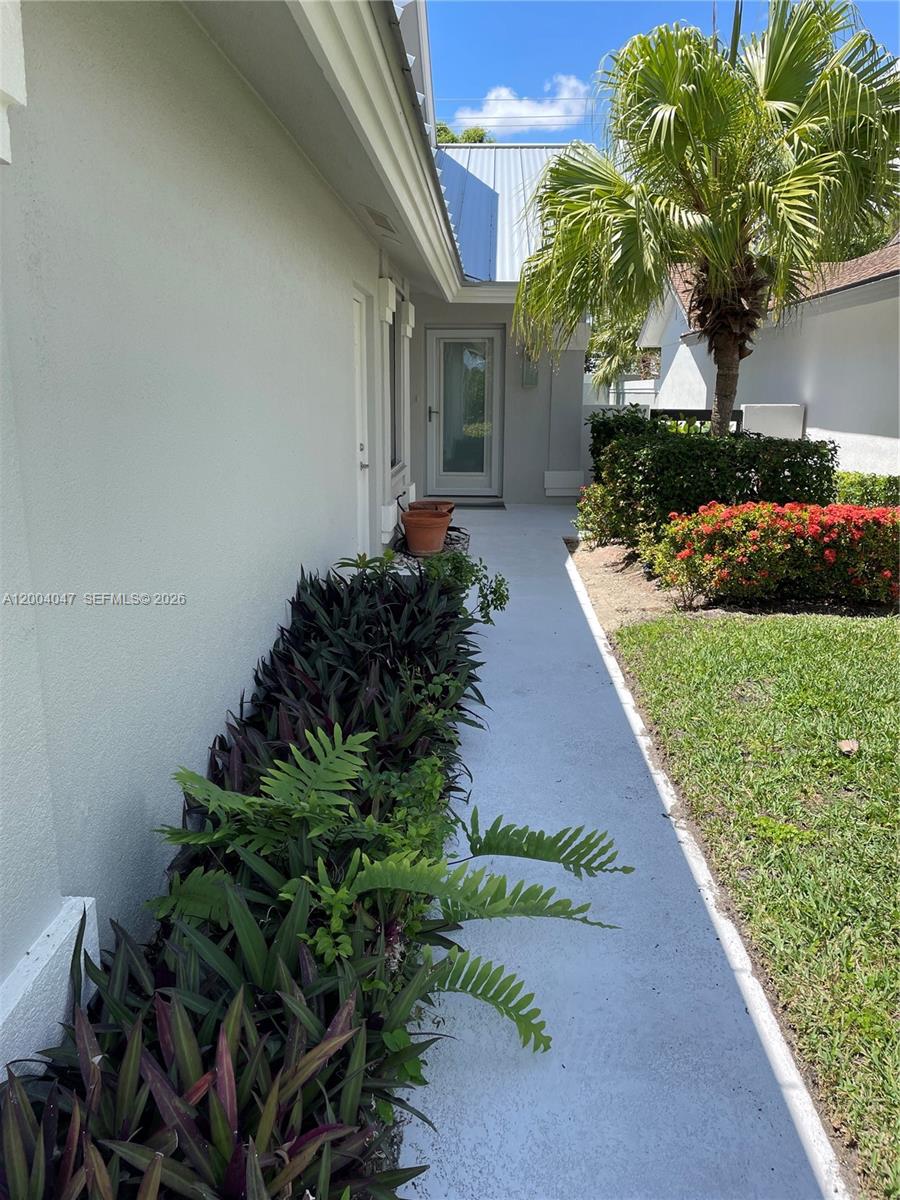 A concrete walkway leads along the side of a house toward a glass door — 126 Ocean PInes Terrace # 126, Jupiter FL 33477, JUPITER, FL