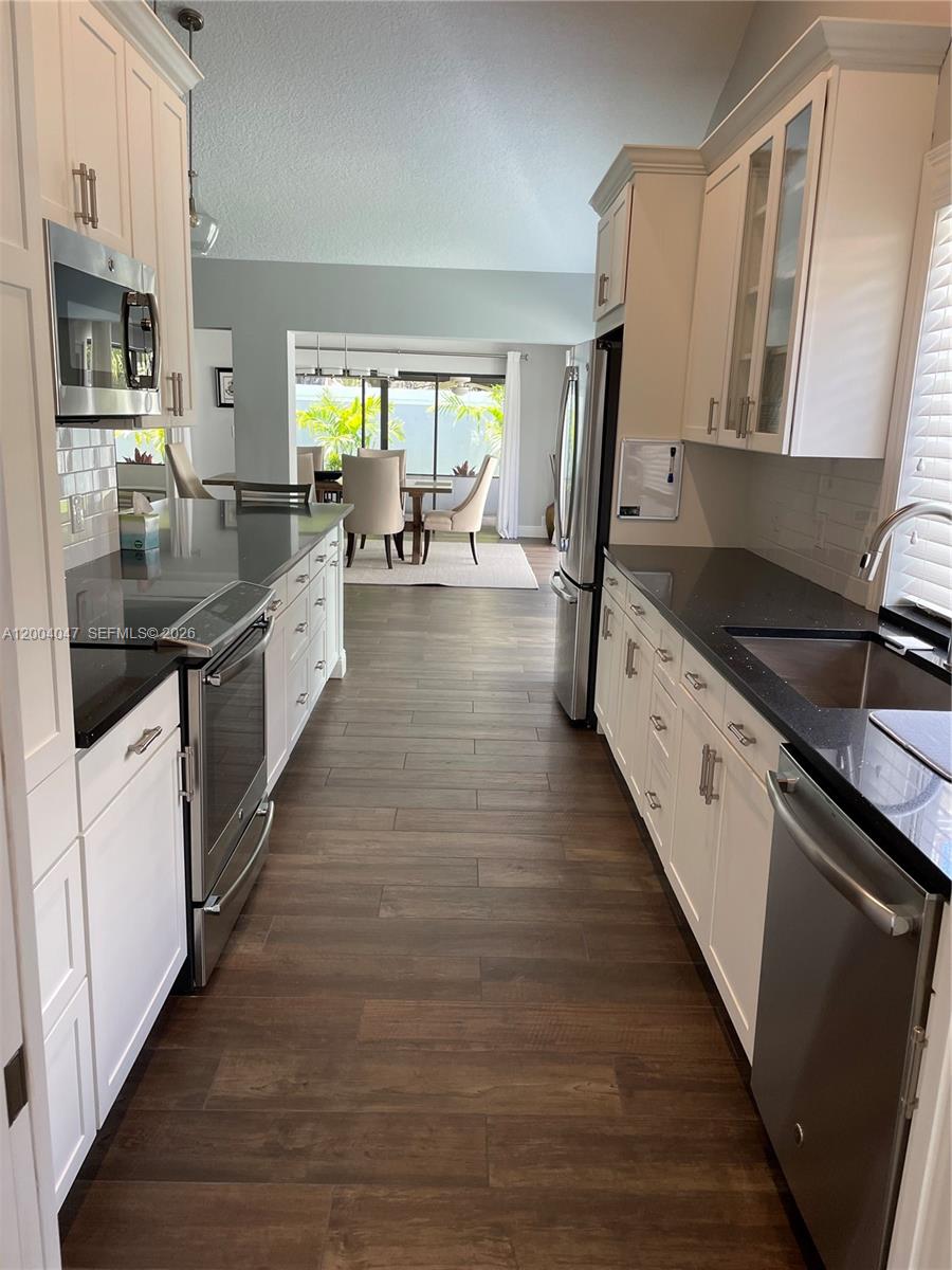 A galley kitchen features white cabinets, dark countertops, stainless steel appliances, and wood-look flooring — 126 Ocean PInes Terrace # 126, Jupiter FL 33477, JUPITER, FL
