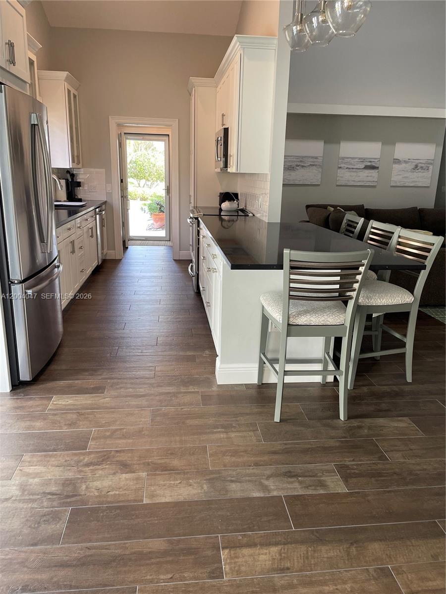 A kitchen features white cabinets, black countertops, stainless steel appliances, and wood-look tile flooring — 126 Ocean PInes Terrace # 126, Jupiter FL 33477, JUPITER, FL
