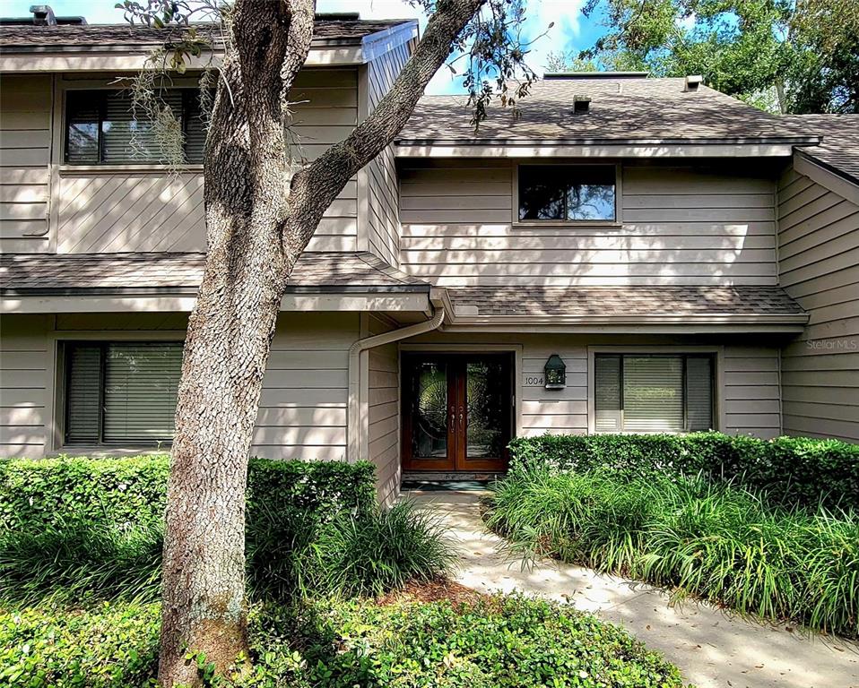 A two-story house with tan horizontal siding, a double front door, and surrounding landscaping — 1004 OLD MILL POND ROAD, PALM HARBOR, FL
