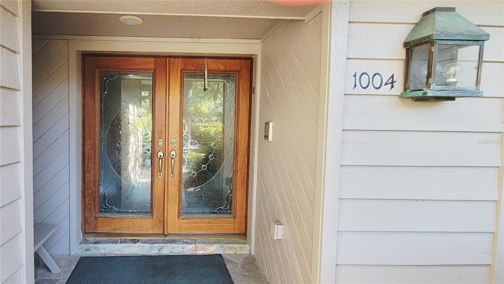 A front entryway features double wooden doors with decorative glass panels and a wall-mounted lantern — 1004 OLD MILL POND ROAD, PALM HARBOR, FL