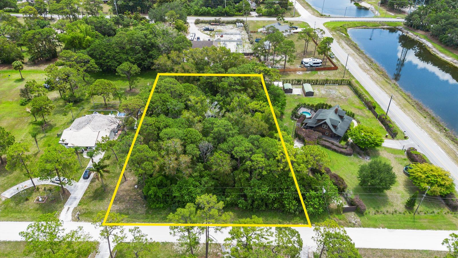 An aerial view shows a rectangular, tree-covered vacant lot outlined in yellow between two houses — Tbd 122nd Drive N, FL 33411, FL