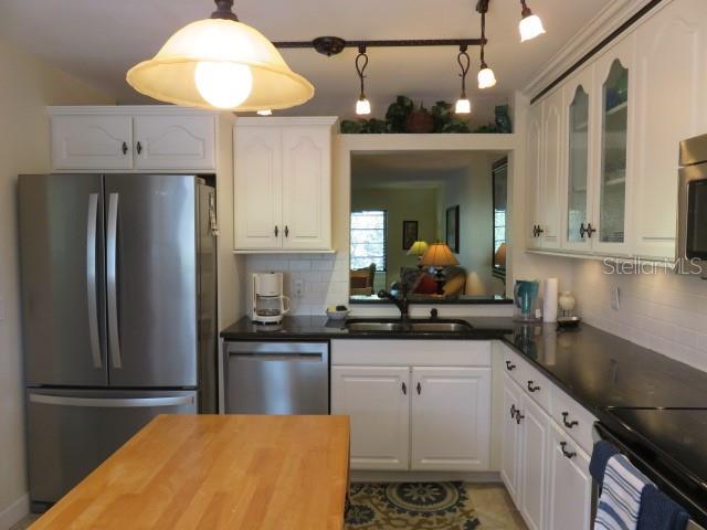 A kitchen with white cabinets, stainless steel appliances, black countertops, and a wooden island — 142 PINENEEDLE DRIVE UNIT 142U, BRADENTON, FL