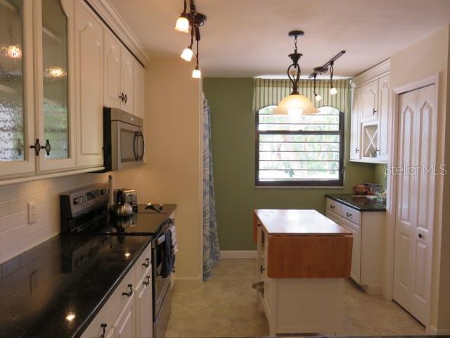 A kitchen features white cabinets, black countertops, a small wooden island, and a green accent wall — 142 PINENEEDLE DRIVE UNIT 142U, BRADENTON, FL