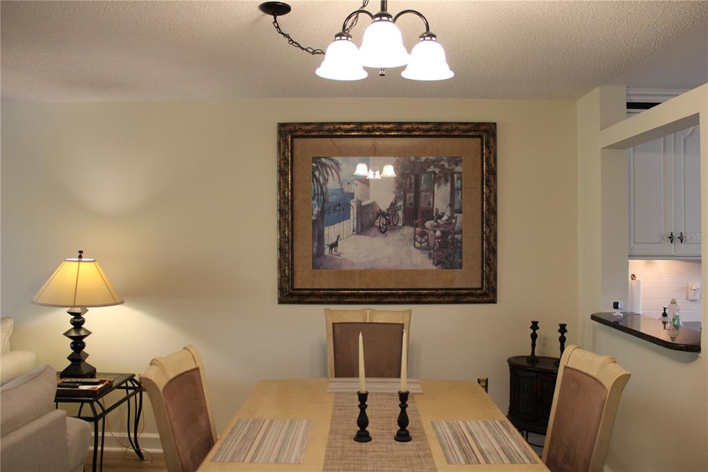 A dining room features a wooden table, four chairs, a chandelier, and framed wall art — 142 PINENEEDLE DRIVE UNIT 142U, BRADENTON, FL