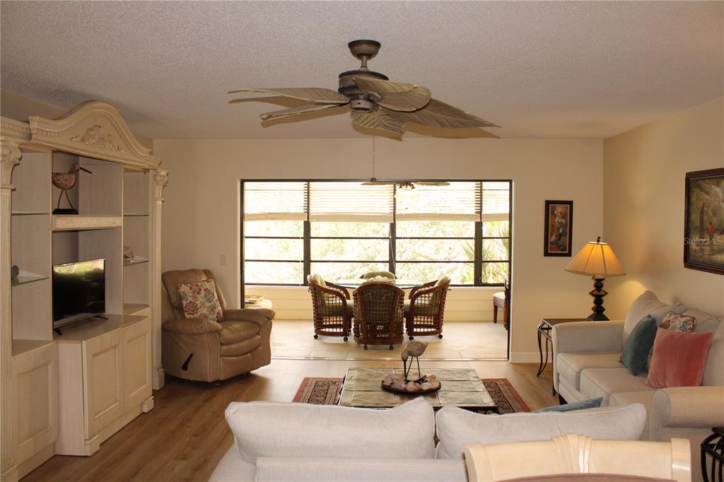 A living room with a ceiling fan, light-colored furniture, and a view of a screened porch — 142 PINENEEDLE DRIVE UNIT 142U, BRADENTON, FL