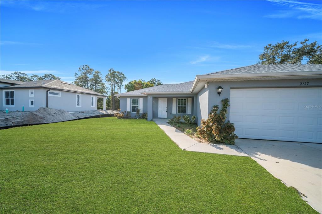 A single-story house with a gray exterior, a white garage door, and a green lawn — 2617 53RD ST W, LEHIGH ACRES, FL