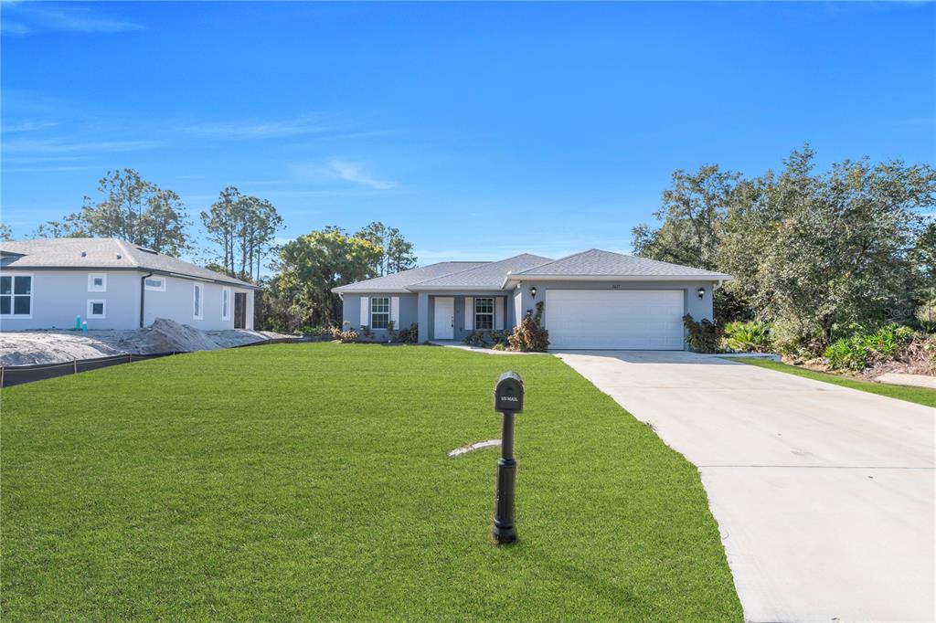 A single-story house with a white garage and a large front lawn under a blue sky — 2617 53RD ST W, LEHIGH ACRES, FL