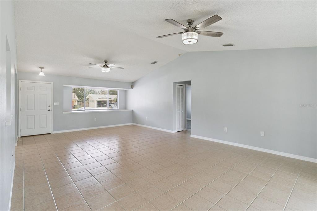 A spacious living room features light-colored tile flooring, vaulted ceilings with two fans, and windows — 940 FOREST STREET NE, PALM BAY, FL