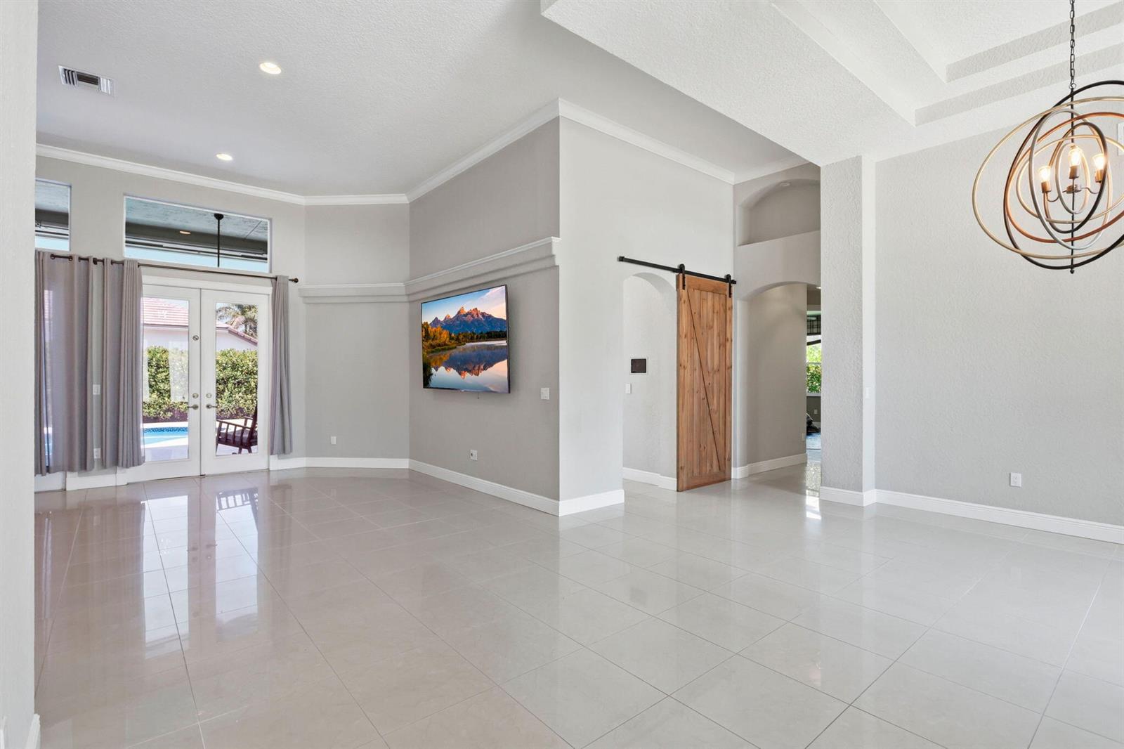 A bright living room features light tile floors, a wall-mounted television, and a wooden barn door — 21653 Marigot Drive, Boca Raton FL 33428, BOCA RATON, FL