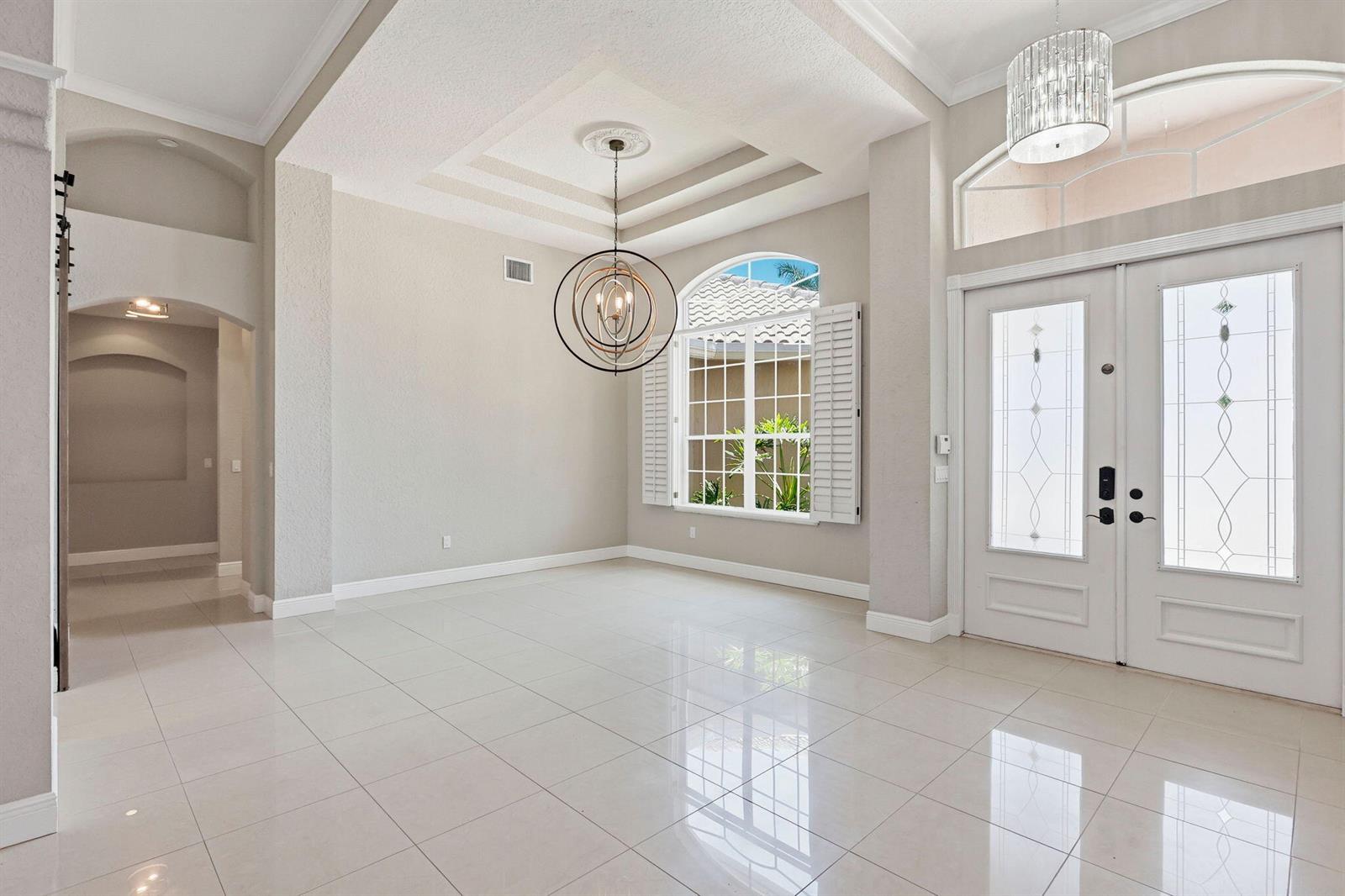 A bright foyer features white tile floors, a modern orb chandelier, and double entry doors — 21653 Marigot Drive, Boca Raton FL 33428, BOCA RATON, FL