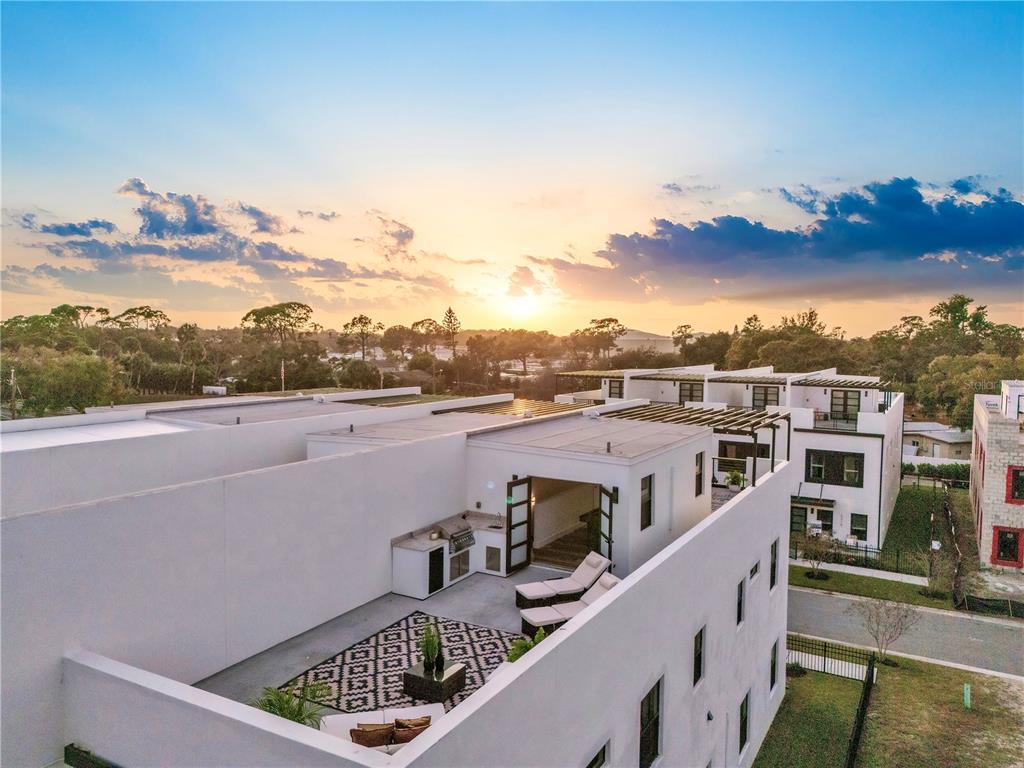 An aerial view of a modern rooftop terrace featuring a kitchenette, lounge chairs, and rug — 6222 64TH WAY N, PINELLAS PARK, FL