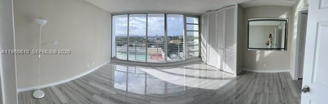 A bright room features light wood-look flooring, a floor lamp, large windows, and mirrored closet doors — 1720 Harrison St # 9A, Hollywood FL 33020, HOLLYWOOD, FL