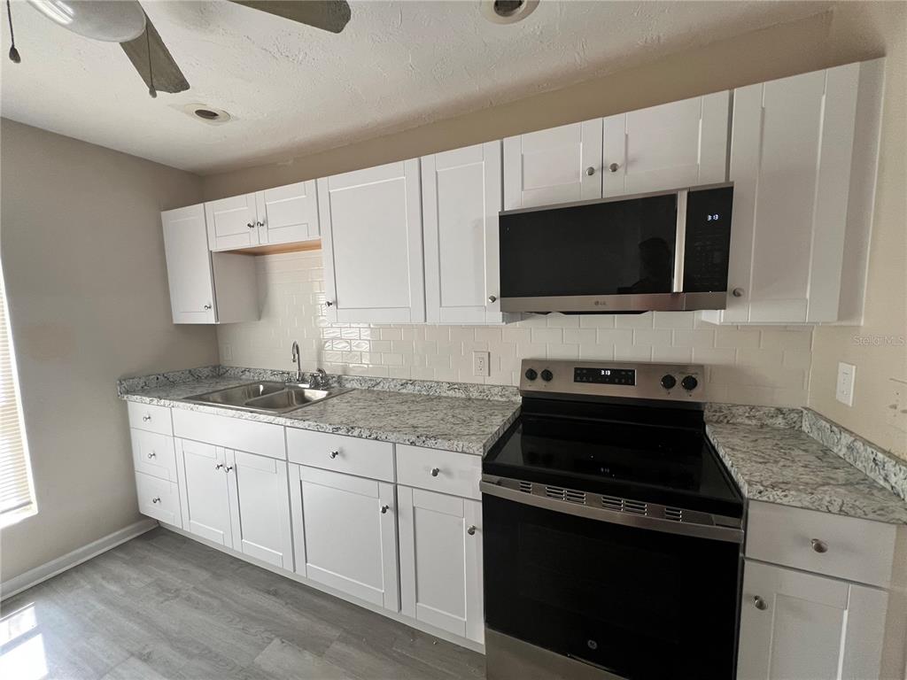 A kitchen features white cabinets, granite countertops, a stainless steel microwave, and a black stove — 408 HENRY BUTTS DRIVE, DAYTONA BEACH, FL