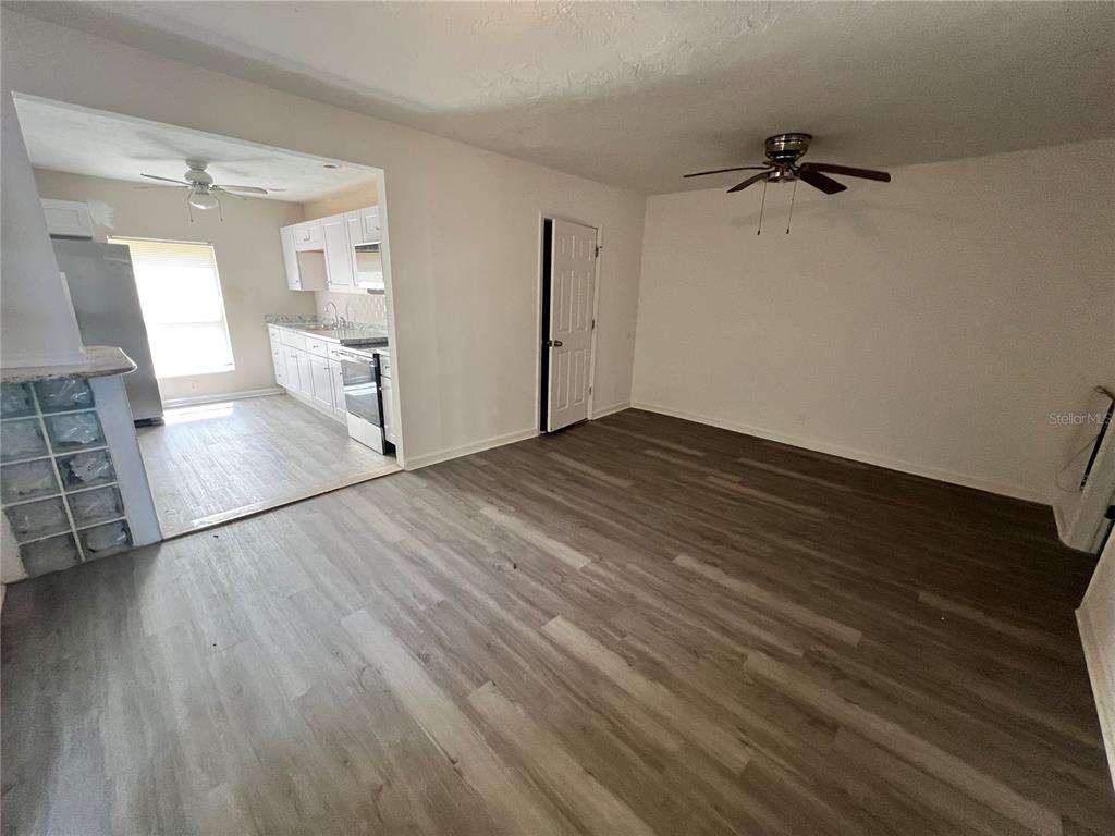 A living room with wood-look flooring connects to a kitchen featuring white cabinets and appliances — 408 HENRY BUTTS DRIVE, DAYTONA BEACH, FL