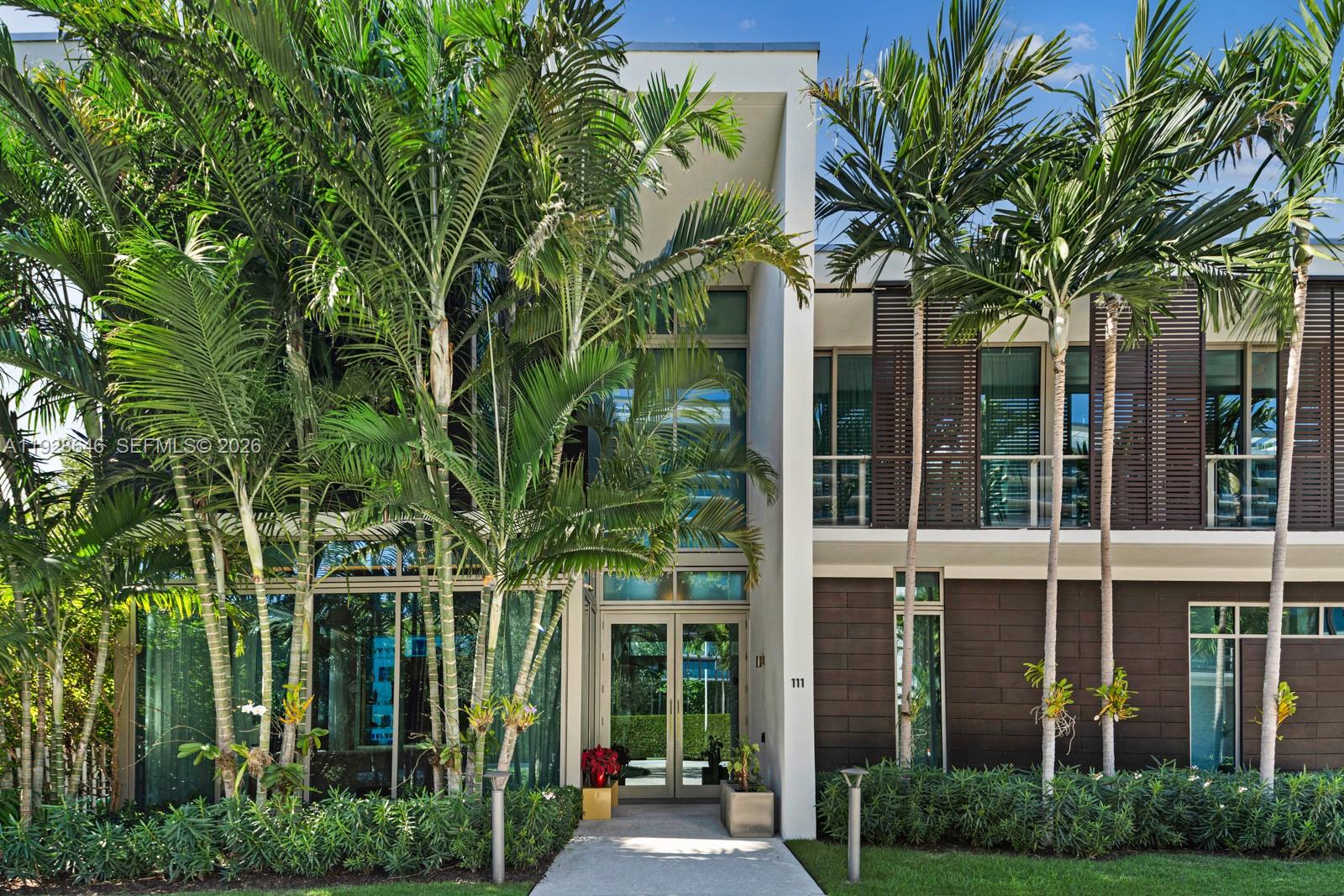 A modern two-story house exterior features a glass entrance, dark wood paneling, and tall palm trees — 111 Reef Ln, Key Biscayne FL 33149, KEY BISCAYNE, FL