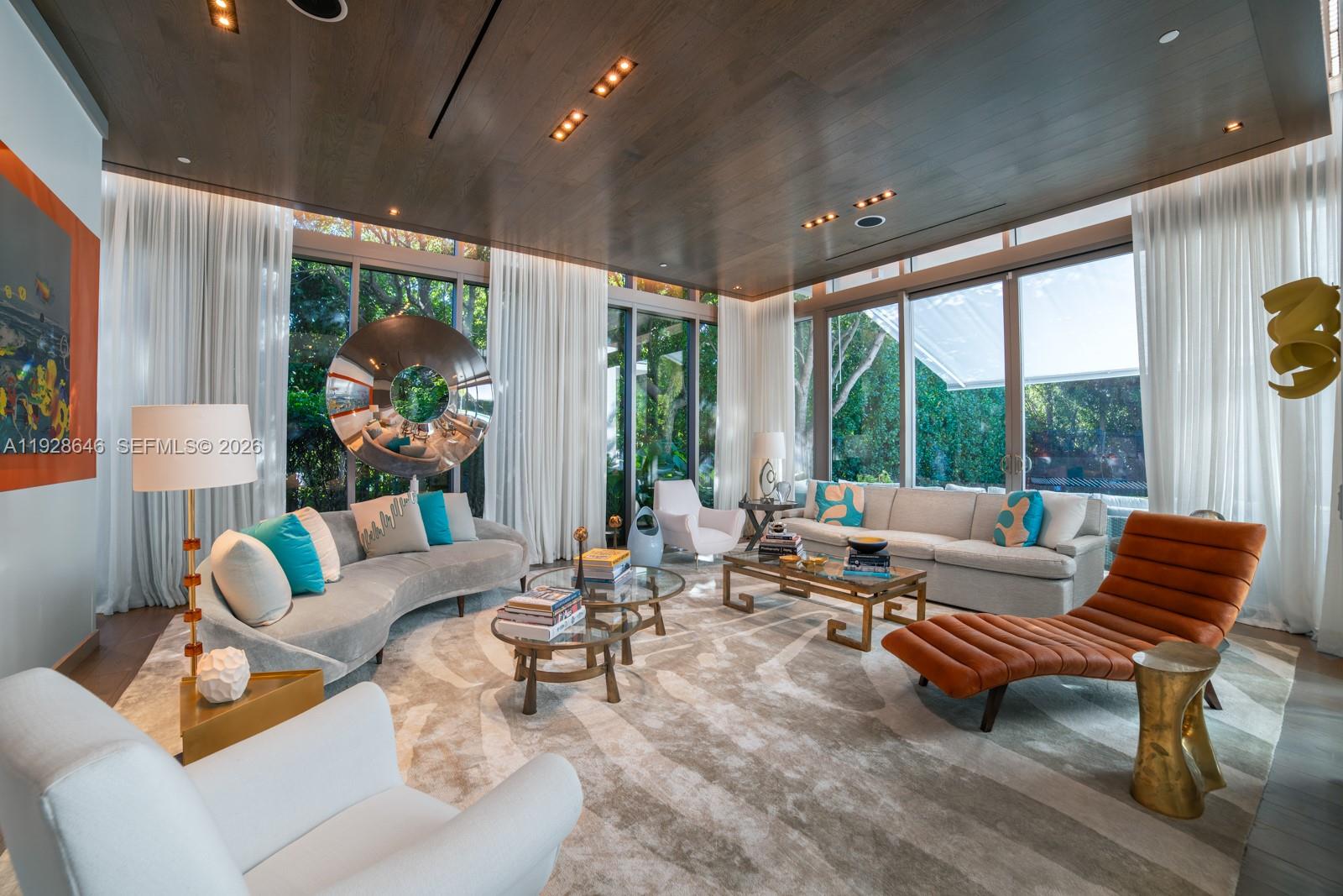 A modern living room features a curved sofa, an orange chaise lounge, and floor-to-ceiling windows — 111 Reef Ln, Key Biscayne FL 33149, KEY BISCAYNE, FL