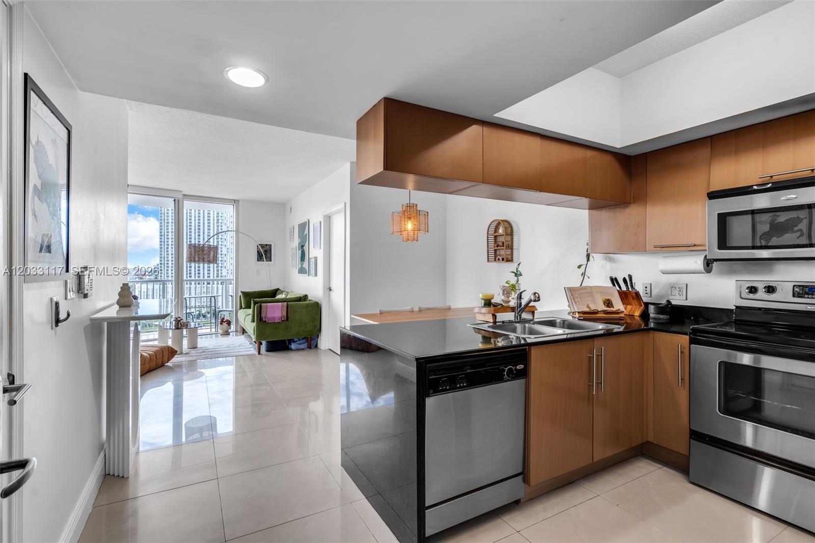 A modern kitchen with wood cabinets and black countertops opens into a bright living area — 1750 N Bayshore Dr # 1815, Miami FL 33132, MIAMI, FL