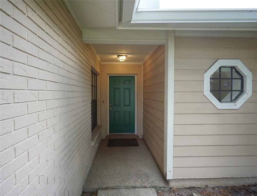 A recessed entryway features a green front door, brick and siding walls, and a window — 8755 HAMPDEN DRIVE, TAMPA, FL