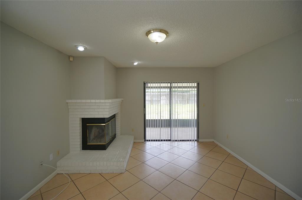 A living room features a white brick corner fireplace, tile flooring, and sliding glass doors — 8755 HAMPDEN DRIVE, TAMPA, FL