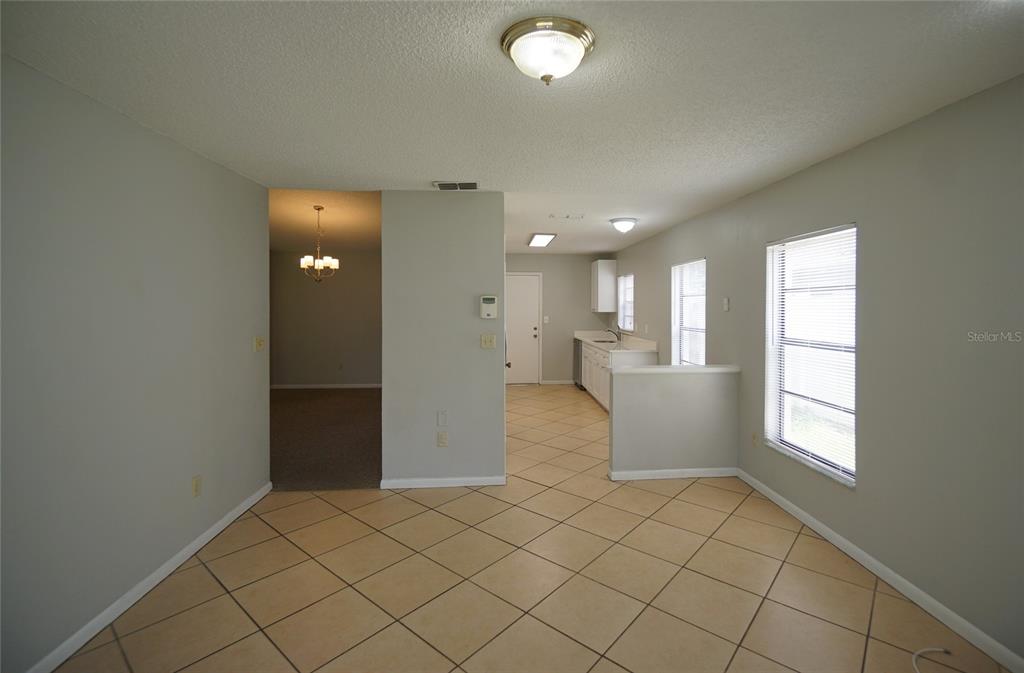 A dining area with tile flooring leads to a kitchen and a carpeted living space — 8755 HAMPDEN DRIVE, TAMPA, FL