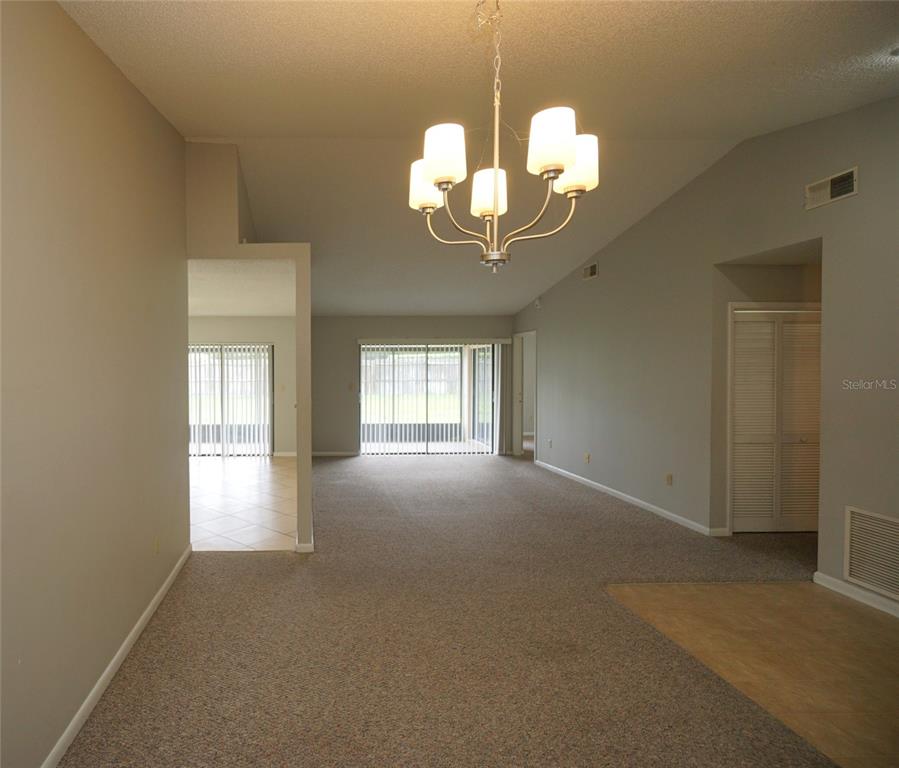 A living room with carpeted floors, a vaulted ceiling, and a central chandelier — 8755 HAMPDEN DRIVE, TAMPA, FL
