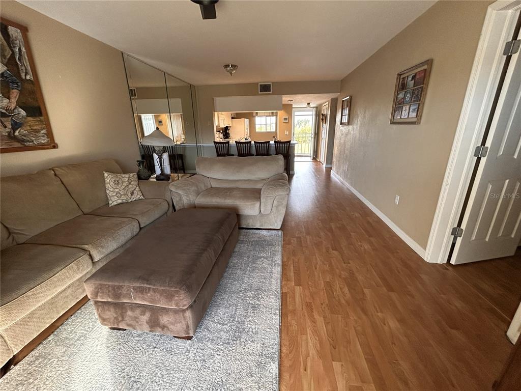 A living room features light wood flooring, a beige sofa, and a kitchen in the background — 3310 LOVELAND BOULEVARD UNIT 1705, PUNTA GORDA, FL