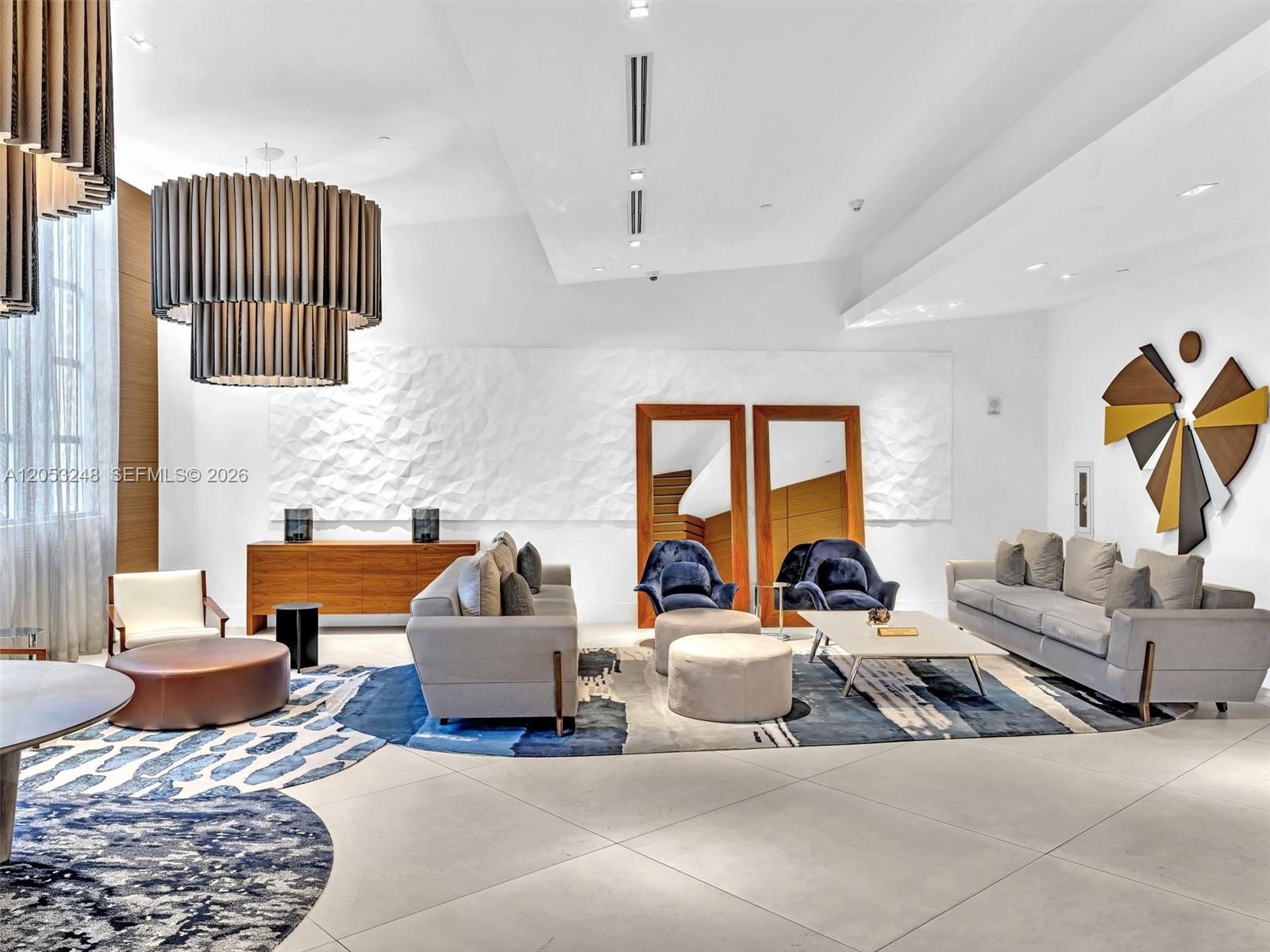 A modern living room features two grey sofas, blue accent chairs, and large tiered chandeliers — 3301 NE 1st Ave # H2706, Miami FL 33137, MIAMI, FL