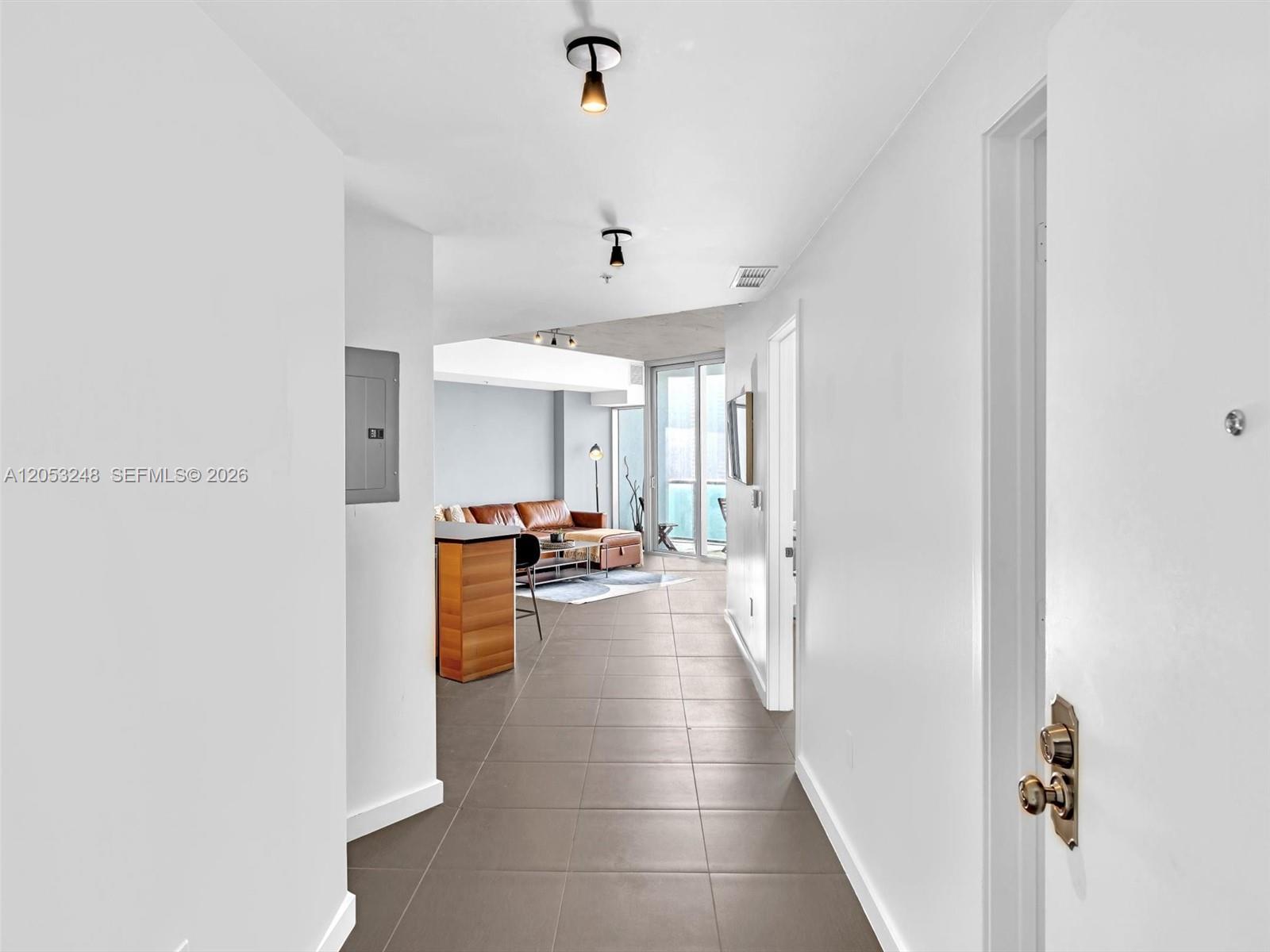 A tiled hallway leads into a living area with a leather sofa and balcony access — 3301 NE 1st Ave # H2706, Miami FL 33137, MIAMI, FL