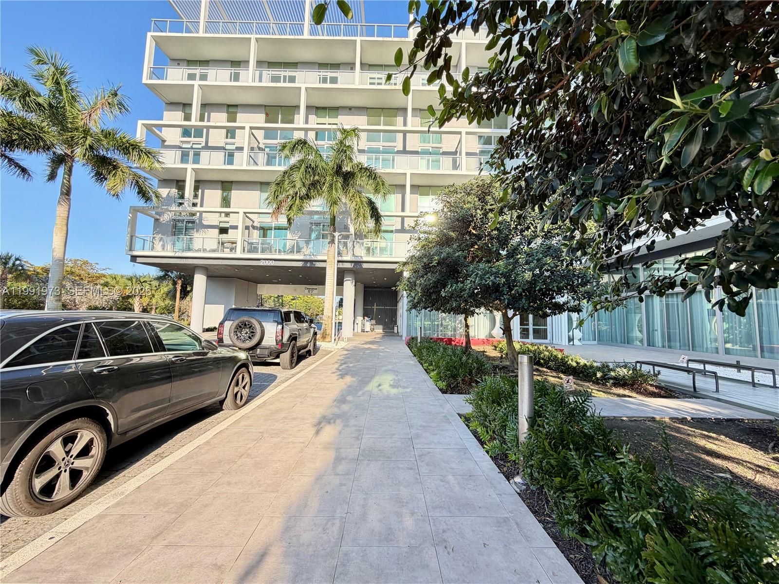 A modern multi-story building exterior features balconies, palm trees, and a paved walkway — 2000 metropica way # 2208, Sunrise FL 33323, SUNRISE, FL