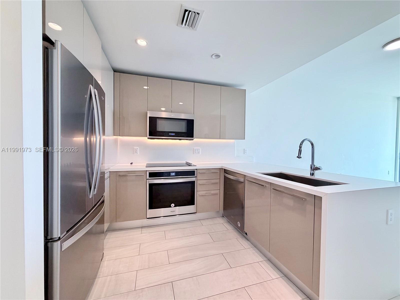 A modern kitchen features glossy taupe cabinets, stainless steel appliances, and white countertops — 2000 metropica way # 2208, Sunrise FL 33323, SUNRISE, FL