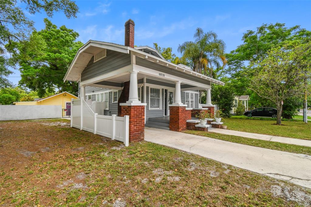 A gray bungalow with a brick-based front porch and a white fence sits outside — 6810 N NAVIN AVENUE, TAMPA, FL