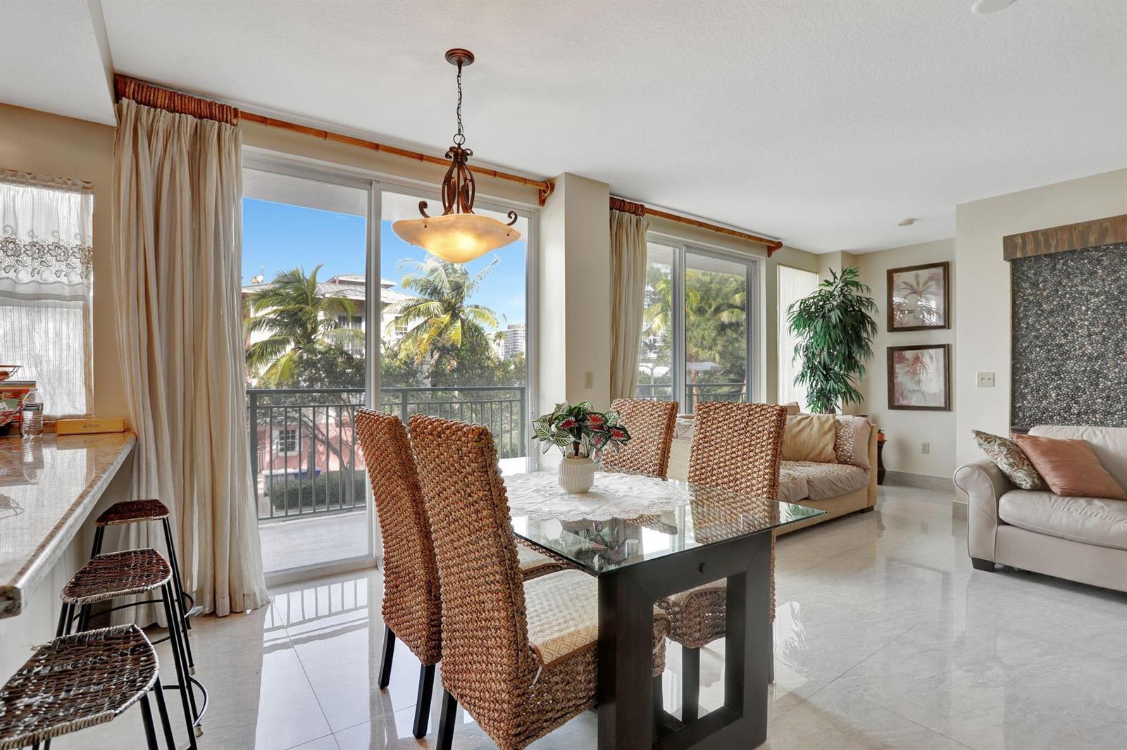 A dining area with a glass table and wicker chairs sits beside a living room — 3210 NE 5th Street # 202, Pompano Beach FL 33062, POMPANO BEACH, FL