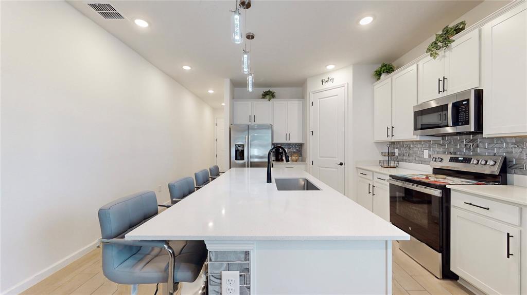 A modern kitchen features a long white island, grey bar stools, and white cabinetry — 2303 JAGGER LANE, EAGLE LAKE, FL