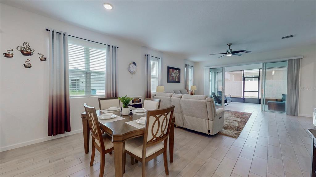 An open-concept dining and living area features light tile floors, a wooden table, and sliding doors — 2303 JAGGER LANE, EAGLE LAKE, FL