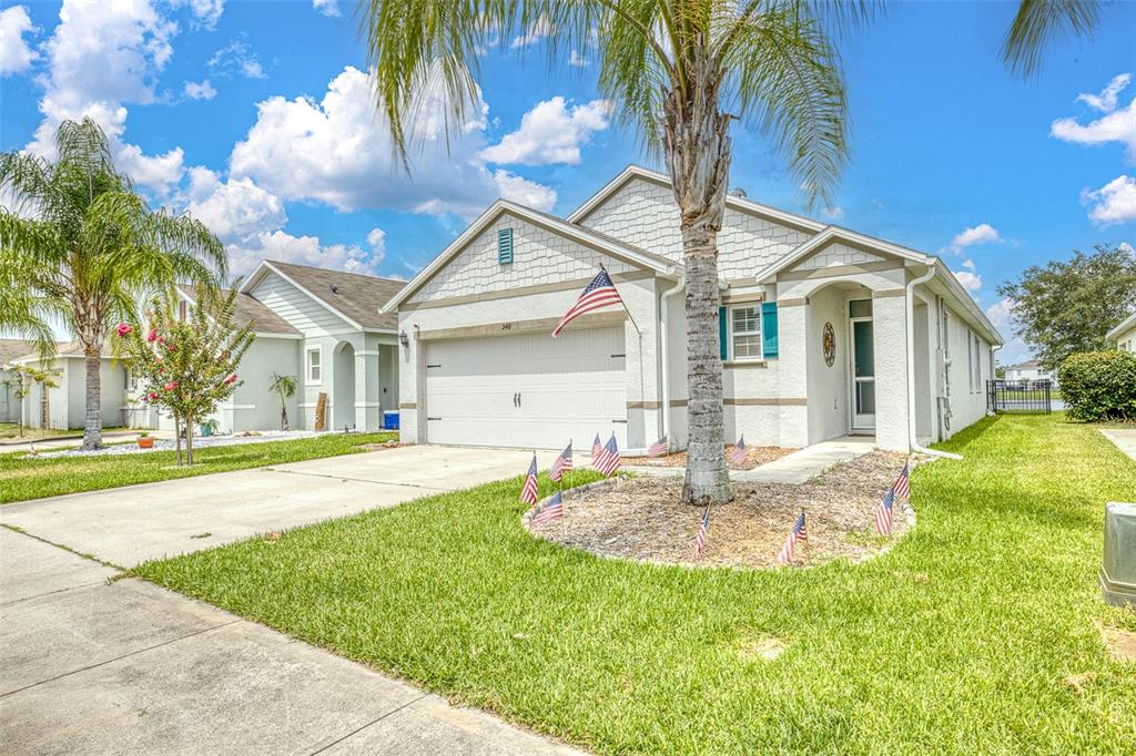 A single-story house with a white garage, palm tree, and American flags in the yard — 548 ARMOYAN WAY, NEW SMYRNA BEACH, FL
