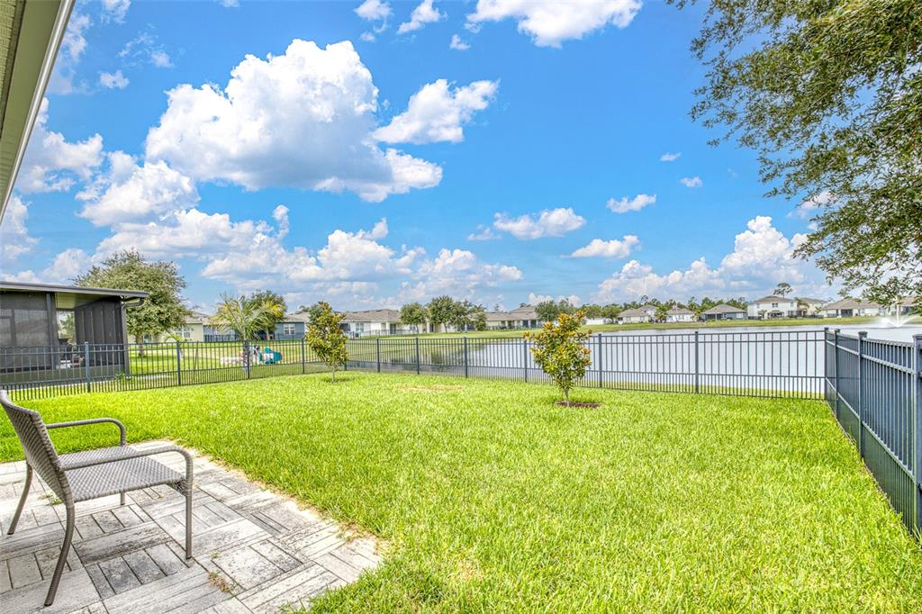 A backyard with a paved patio, a chair, two small trees, and a metal fence — 548 ARMOYAN WAY, NEW SMYRNA BEACH, FL