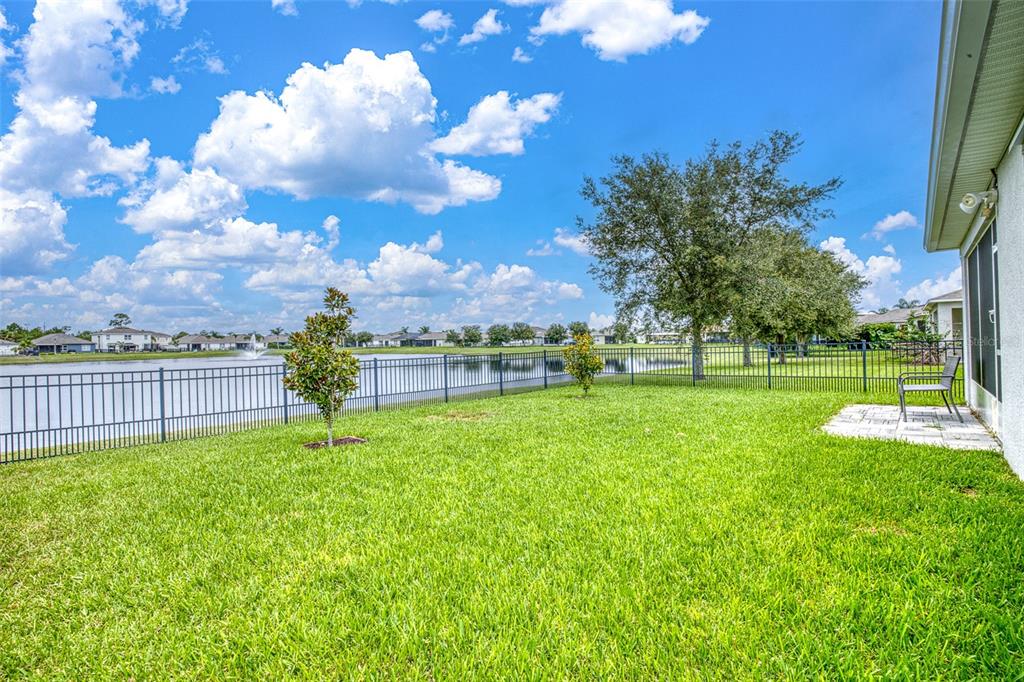 A grassy backyard features a metal fence, a small patio, and a view of a lake — 548 ARMOYAN WAY, NEW SMYRNA BEACH, FL
