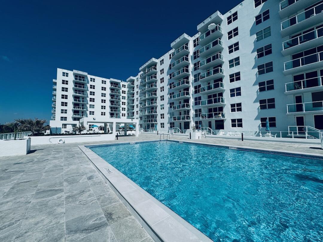 A swimming pool sits on a stone patio in front of a large white apartment building — 3450 S Ocean Boulevard # 5030, Palm Beach FL 33480, PALM BEACH, FL